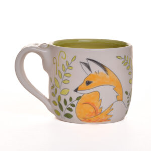 Small mug decorated with foxes and ferns. When artist Meghan Bernard created this design, she was inspired by a pair of foxes that moved in around her studio. The carvings are so sweet and whimsical. Each piece is thrown porcelain on the wheel and then carved. After each piece dries, she inlays the carving with black slip and then hand paints the rest of the colors.