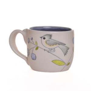 Small mug decorated with birds and blueberries. The carvings are so sweet and whimsical. Each piece is thrown porcelain on the wheel and then carved. After each piece dries the black lines are carved into the porcelain with a sharp knife, then inlaid with black under-glaze. Each color is hand painted before being glazed with food safe glazes.