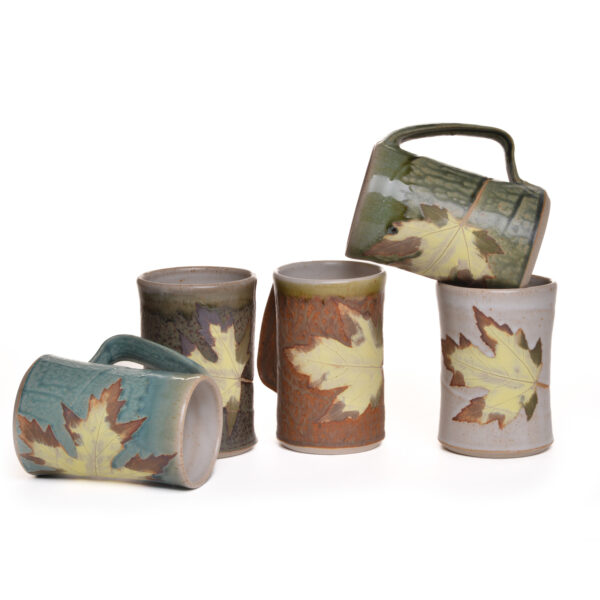 Wheel-thrown mug with leaf decoration. Artist Travis Berning creates his unique, one-of-a-kind mugs on the potter's wheel, then adds a leaf decoration and handle. The mugs are dipped in a wood-ash glaze with white interior.