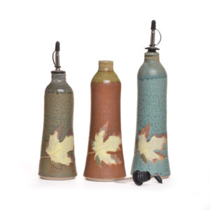 Wheel-thrown oil cruet with metal spout. Artist Travis Berning creates his cruets on the potter’s wheel, then adds a leaf decoration.. Artist Travis Berning creates his cruets on the potter's wheel, then adds a leaf decoration.