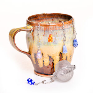 These unique and colorful handmade glass tea infusers are like jewelry for your tea time! Each stainless steel fine mesh ball features 3 handmade glass beads that dangle elegantly over a mug. Teresa Brittain creates glass beads over a torch, using the centuries-old technique of lampworking, then combines the beads with sterling silver findings and chains to create unique pieces of wearable art. *Hand rinse and dry after each use to prevent wear. Do not place in dishwasher*