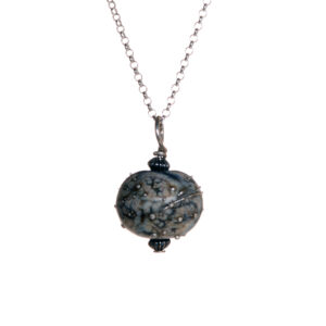 Mini black/ivory glass bead with frit pendant created over a torch. Teresa Brittain creates glass beads over a torch, using the centuries-old technique of lampworking, then combines the beads with sterling silver findings and chains to create unique pieces of wearable art.