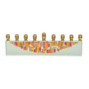 Menorah fused in red and orange toned glass, with dichroic speckles. Artist Alicia Kelemen fuses the colorful glass together, then laminates it to a glass surface in a light greenish tone, and adds silver metal tops.