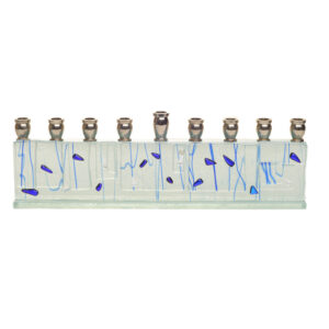 Menorah fused in clear glass with blue lines, with silver and blue dichroic speckles. Artist Alicia Kelemen fuses the colorful glass together, then laminates it to a glass surface in a light greenish tone, and adds silver metal tops.
