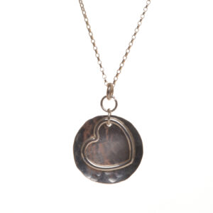 Handcrafted sterling silver heart on sterling silver hammered disc pendant featuring a free flowing heart dancing on a brilliantly shining disc. Designed and crafted by silversmith Suzanne Farran-Hrytzik of North Carolina. Great for everyday wear. Expect slight variations in design. Matching earrings available. 