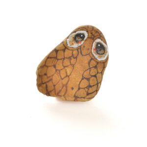 Hand painted river rock owl pin by Mänya Pirkle of Tennessee. Each pin features a natural river stone sourced from the mountains, transformed into a whimsical owl with unique features. No two owls are exactly alike, making each pin a special, wearable piece of folk art.