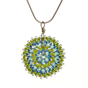 Round disc necklace featuring handwoven glass seed beads by jeweler Leslie Fawcett of Tennessee. With a needle and nylon thread, Leslie takes tiny glass seed beads and weaves them into larger beads that are then rolled up and sewn together. The use of the peyote stitch allows the ends of the rectangle to interlock when sewn together, and repeated passes through the beads reinforce the whole. Different colors available.