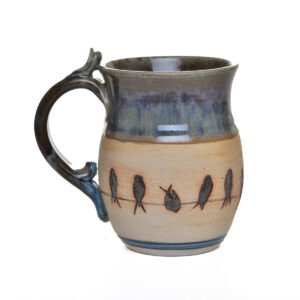 This handcrafted stoneware mug features delicately etched birds perched on a wire, created by North Carolina potter Rebecca Regal. Her ceramics combine hand-building, wheel-throwing, and sculptural techniques, drawing inspiration from Appalachian nature, folklore, and rustic charm. Most of the glazes she uses are original glaze recipes curated by her potter father for over 50 years.. Each piece is produced in small batches and is one of a kind.