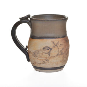 This handcrafted stoneware mug features a delicately etched bird perched on a branch, created by North Carolina potter Rebecca Regal. Her ceramics combine hand-building, wheel-throwing, and sculptural techniques, drawing inspiration from Appalachian nature, folklore, and rustic charm. Most of the glazes she uses are original glaze recipes curated by her potter father for over 50 years.. Each piece is produced in small batches and is one of a kind.