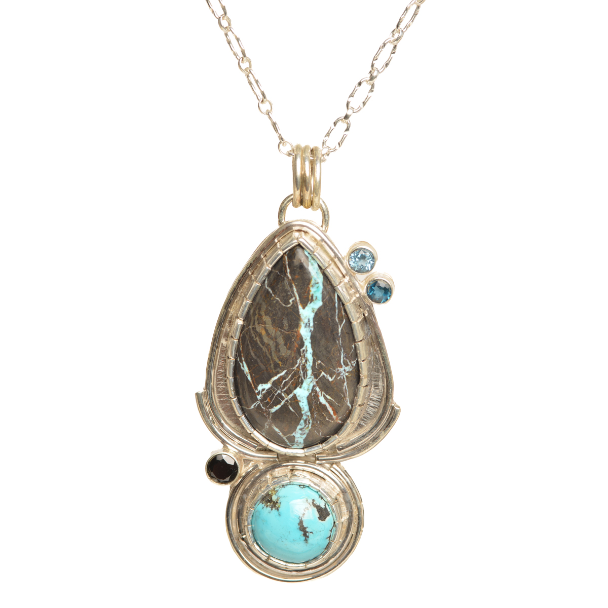 “Blue Lotus” handcrafted sterling silver pendant featuring striking castellated bezel-set Black Jack turquoise accented by a sparkling cluster of faceted black spinel, London blue topaz, and Swiss blue topaz, by Ruthie Cohen of North Carolina.